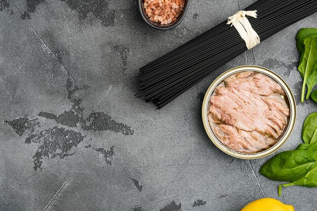 Pasta con set di ingredienti crudi di tonno, su sfondo di tavolo in pietra grigia, vista dall'alto piatta, con spazio di copia per il testo