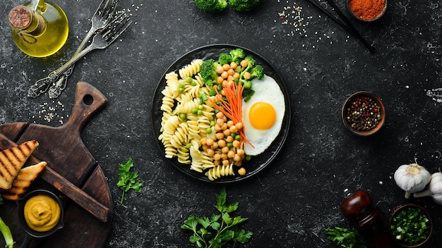 Pasta with vegetables and fried egg on a black stone plate Bowl Buddha Top view Free space for text