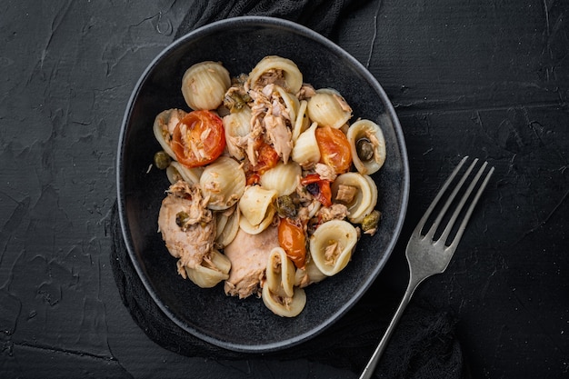 Pasta with vegetables and tuna in bowl, on black table, top view