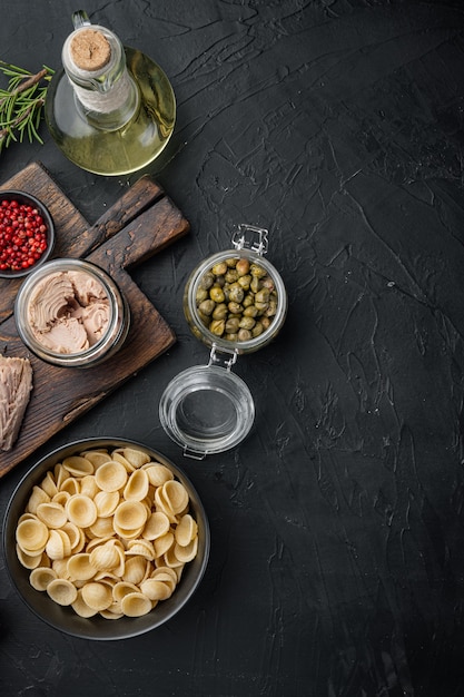 Pasta with vegetables and tuna ingredients on black, top view