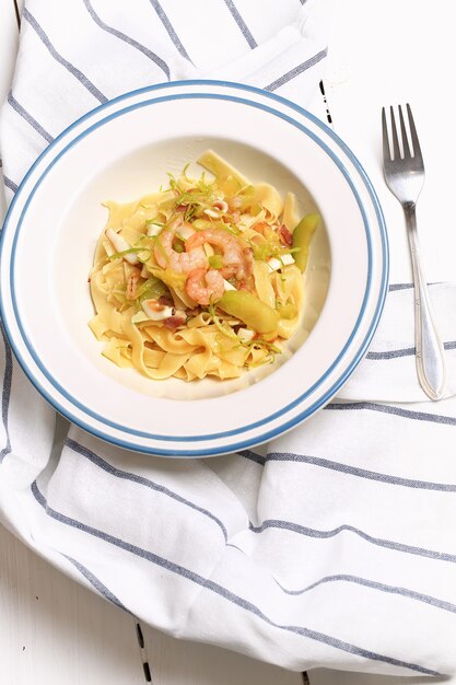 Pasta with zucchini and seafood in a white plate with a fork on a kitchen cloth on white background