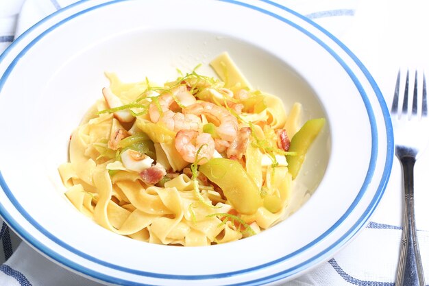 Pasta con zucchine e frutti di mare in un piatto bianco con una forchetta su un panno da cucina su sfondo bianco