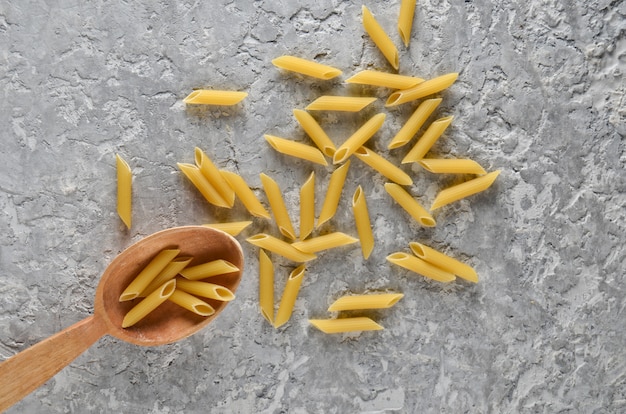 Pasta in a wooden spoon on a gray concrete table.