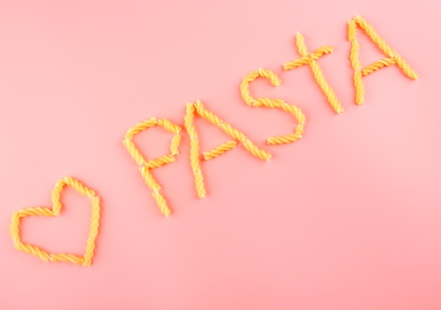 Foto parola di pasta fatta con fusilli su sfondo rosa