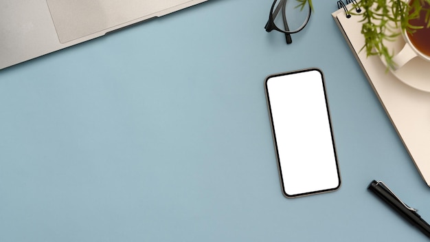 Pastel blue workspace with office accessories mobile phone blank screen mockup and copy space