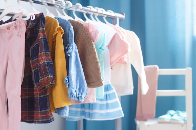 Pastel color children's clothes in a Row on Open Hanger indoors. Clothes for little ladies hung in the children's room.