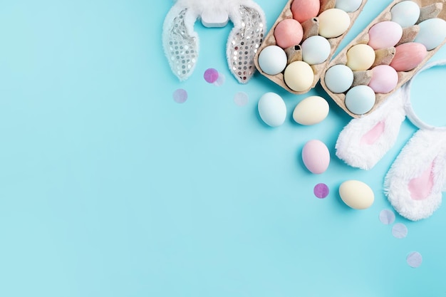 Pastel colored Easter eggs and bunny ears on blue background with copy space