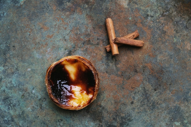 Pastel de nata. Traditional Portuguese dessert egg tart and cinnamon sticks over rustic metal background. Top view