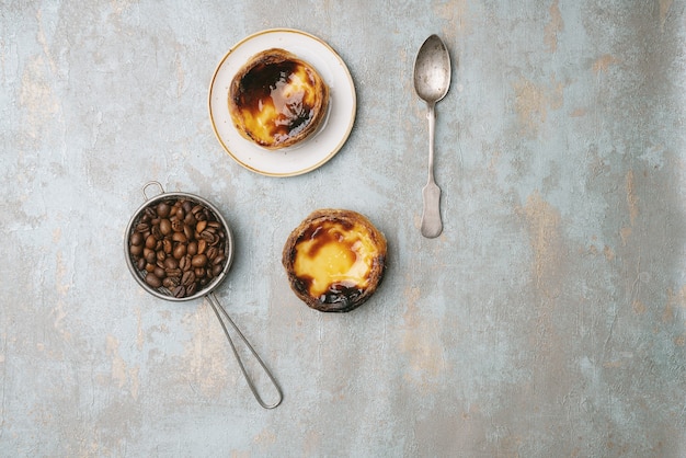 パステルデナタ。伝統的なポルトガルのデザート、プレート上のエッグタルト、素朴な背景の上にローストしたコーヒー豆をストレーナーに入れます。上面図