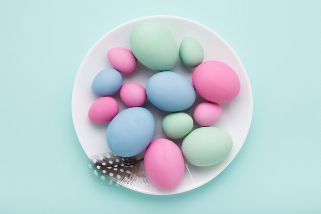 Pastel Easter eggs on white plate on blue background.