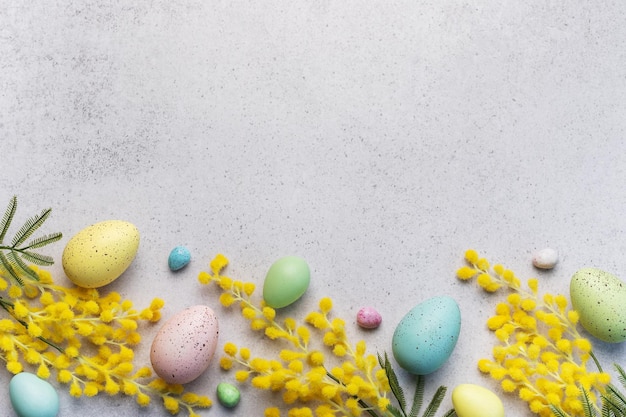 Pastel Easter Eggs and Yellow Mimosa Flowers on a Light Grey Background