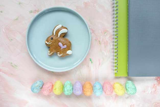 Pastel and gold colored eggs decoration gingerbread Easter bunny cookie and notebooks on pink background Easter celebration concept Top view flat lay copy space