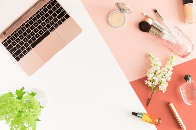 Pastel office table desk with laptop, leaves, spring flowers, clipboard and beauty cosmetic accessories, top view