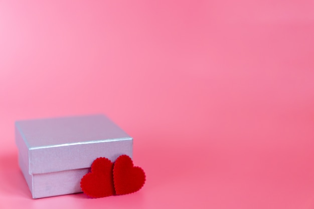 Foto sfondo rosa pastello con una confezione regalo in argento e due forme artigianali a forma di cuore rosso per una persona speciale