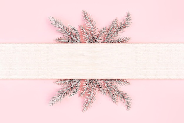 Pastel pink background with snowy fir branches and copy space for text. Christmas, festive or winter background. Top view, flat lay, mock up