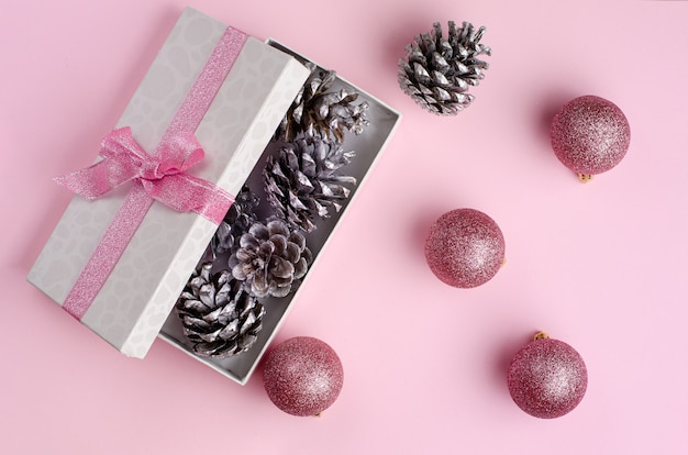 Pastel pink Christmas . Opnened Gift box filled with silver cones and baubles flat lay.