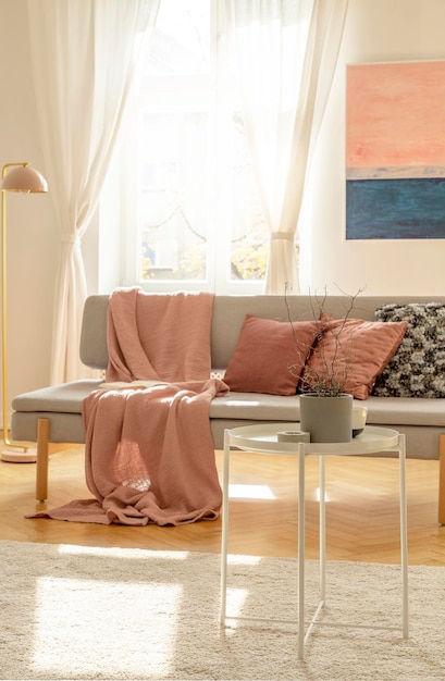 優雅なインテリアの灰色のスカンジナビアのソファにパステルピンクの枕と毛布