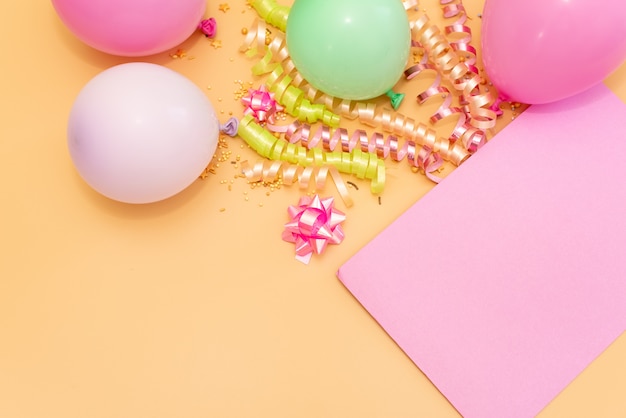 Pastel pink table with frame from balloons and confetti for birthday top view. Flat lay composition.