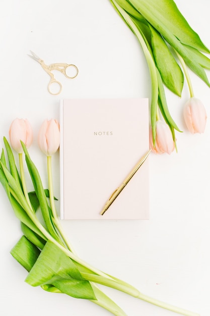 Pastel pink tulip flowers, notebook, golden scissors and pen