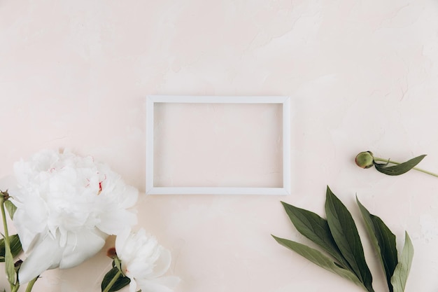 Pastel table with peony flowers and blank white frame with copy space