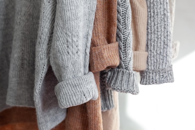 クローゼットにぶら下がっているパステルの暖かいニットの服のセーター居心地の良い秋と冬のワードローブ