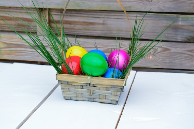 Foto pastelkleur paaseieren in een mand op een witte houten lijst met vers groen gras.