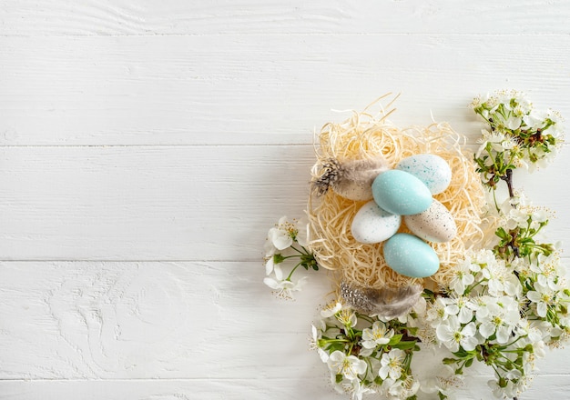 Pastelkleurige paaseieren in nest en lente bloeiende takken op witte houten