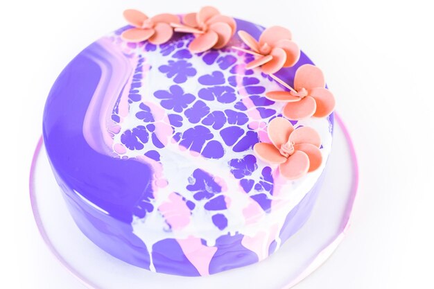 Foto pastre shef che prepara una torta di mousse con glassa a specchio viola e decorata con fiori rosa cioccolato.