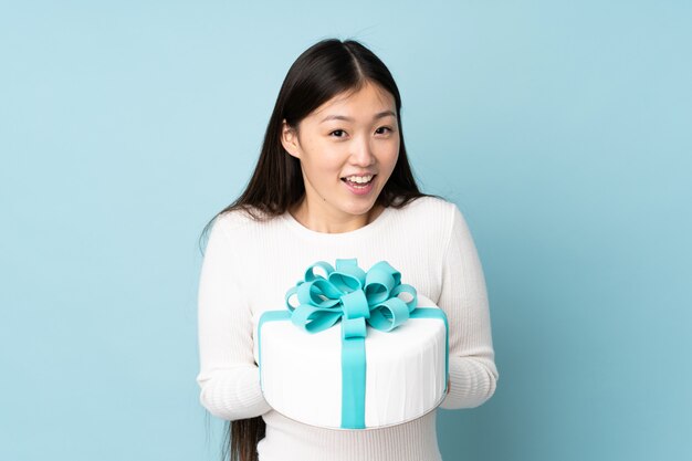 Pastry asian chef holding a big cake on blue wall