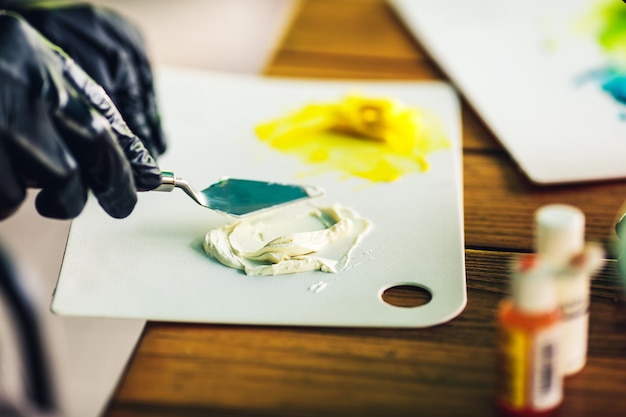 Шеф-кондитер в черных резиновых перчатках перемешивает цветной крем шпателем, чтобы украсить торт пищевым красителем для крема
