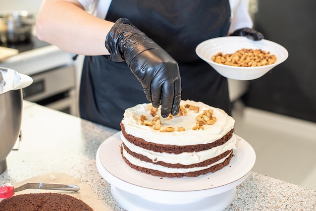 Pastry chef cook confectioner or baker in black gloves and black kitchen apron makes a cake. Home made birthday cake. Concept of homemade pastry, cooking cakes, hobby. Female small home business.