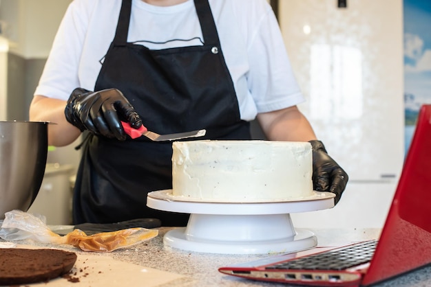 Pastry chef cook confectioner or baker in black gloves and black kitchen apron makes a cake. Home made birthday cake. Concept of homemade pastry, cooking cakes, hobby. Female small home business.