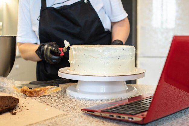 パティシエは、黒い手袋と黒いキッチンエプロンで菓子職人またはパン屋を調理してケーキを作ります。自家製バースデーケーキ。自家製ペストリー、クッキングケーキ、趣味のコンセプト。女性の小さな在宅ビジネス。