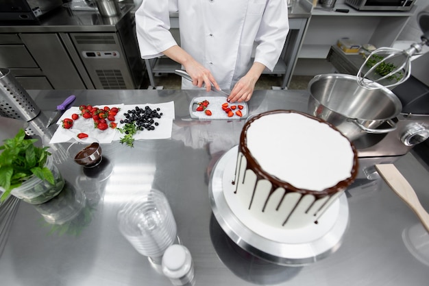 Pastry chef cuts strawberries to decorate the cake