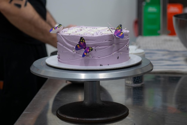 Pastry chef decorating a purple frosted birthday cake with text topping sprinkles pearls and butterflies