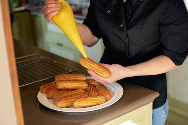 Pastry chef fills the eclairs with cream close up