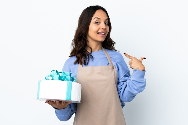 Pastry chef holding a big cake over isolated white wall giving a thumbs up gesture