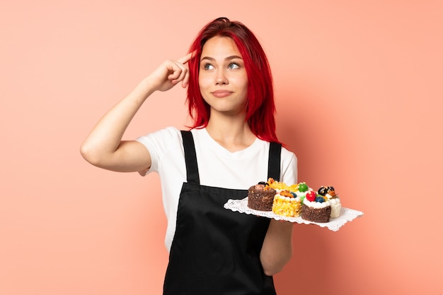 Pastry chef holding a muffins isolated on pink wall having doubts and thinking