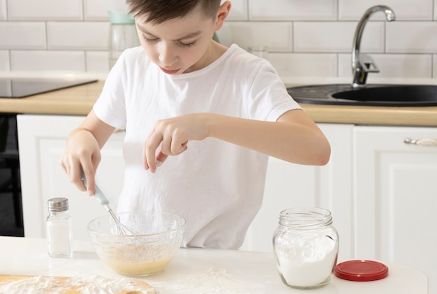 ベーカリーパンのクッキーとケーキを作るパティシエの小さな男の子おいしい甘い食べ物面白い瞬間を自宅のキッチンルームでお楽しみください