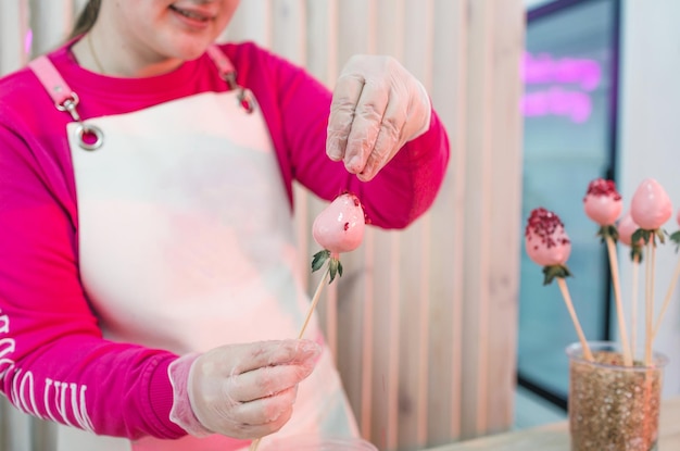 Il pasticciere cosparge le fragole ricoperte di cioccolato con scaglie di cocco colorate. preparazione di dolci. fragole ricoperte di cioccolato