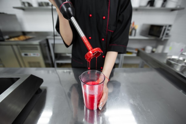 Pastry chef whips up the red mirror icing for the cake with a blender.