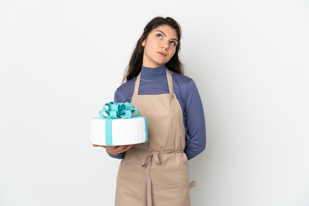 Pastry Russian chef holding a big cake isolated on white wall and looking up