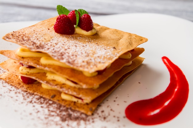 Pastry with leaves of mint. Red sauce and white powder. Dessert that looks appetizing. Raspberry millefeuille is ready.