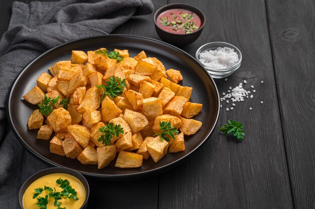 검정색 배경에 뜨거운 소스를 곁들인 Patatas bravas. 스페인 과자인 타파스.