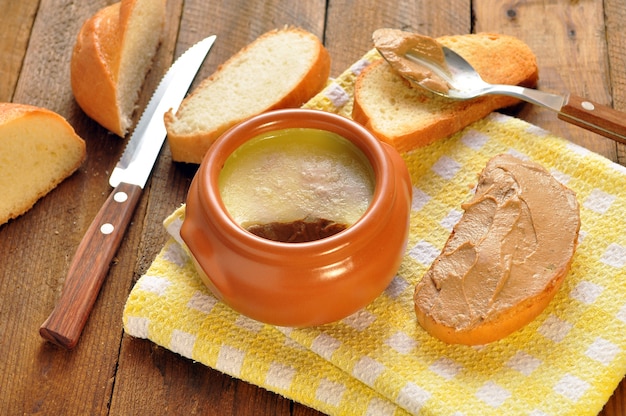 Pate in una pentola di ceramica e tostate la pagnotta su un tovagliolo. cucchiaio e coltello su fondo di legno