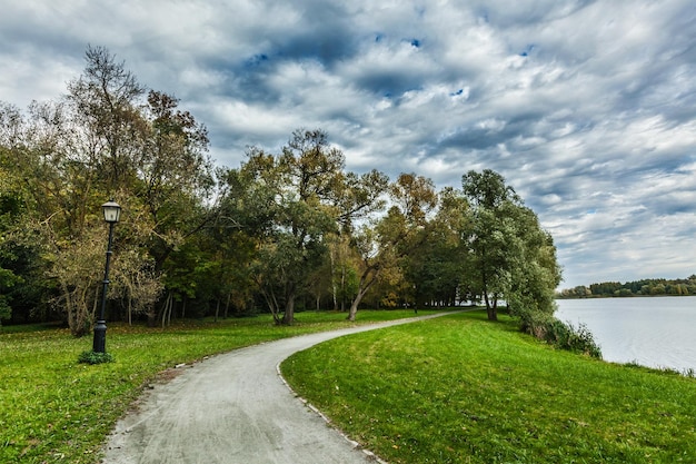 Path in autumn park near the lake with dramatic sky