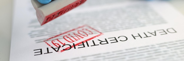 Photo pathologist putting red covid stamp on death certificate closeup