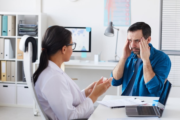 Patient complaining on headache during his visit to the doctor while doctor prescribing him the medicine