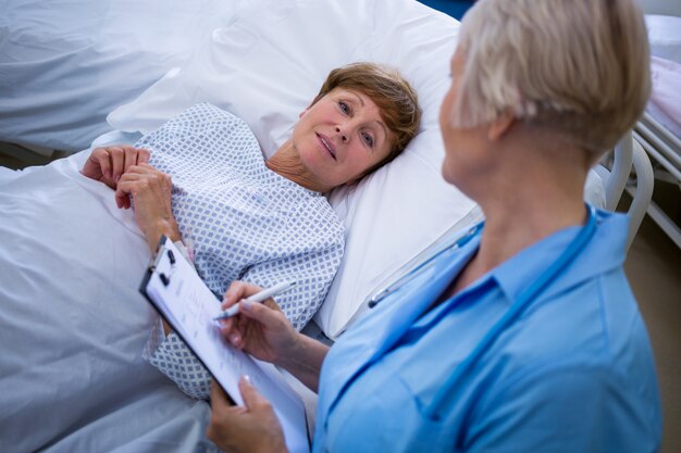 Patiënt die op bed ligt terwijl verpleegster die op klembord schrijft