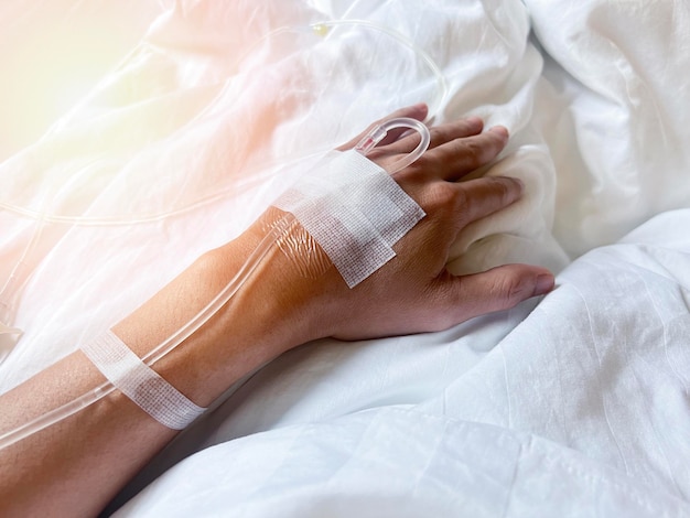 Patient on hospital bed with blurry of Saline intravenous iv drip on hand in hospital Needles and saline tubes are punctured on the patient's hand Health care and Medical equipment concept